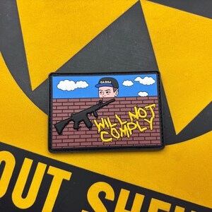 May include: A rectangular morale patch featuring a cartoon character in a blue cap labeled CA DOJ peering over a brown brick wall. A black rifle silhouette is centered on the wall with yellow text reading WILL NOT COMPLY below it.