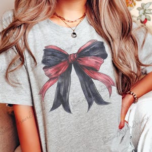 May include: A gray t-shirt with a large, red and black bow graphic printed on the front. The bow is tied with a large, red ribbon.