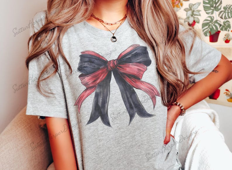 May include: A gray t-shirt with a large, red and black bow graphic printed on the front. The bow is tied with a large, red ribbon.