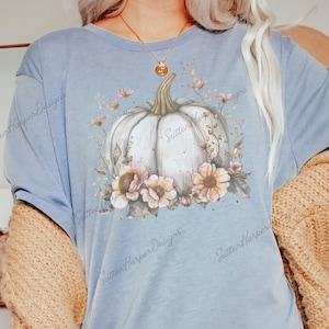 May include: A light blue t-shirt with a white pumpkin surrounded by pink and brown flowers. The text "Sutter Harper Designs" is printed on the shirt.