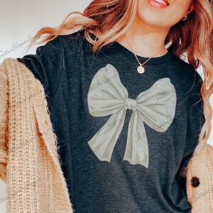 May include: A dark gray t-shirt with a large white bow design. The bow is painted in a watercolor style.