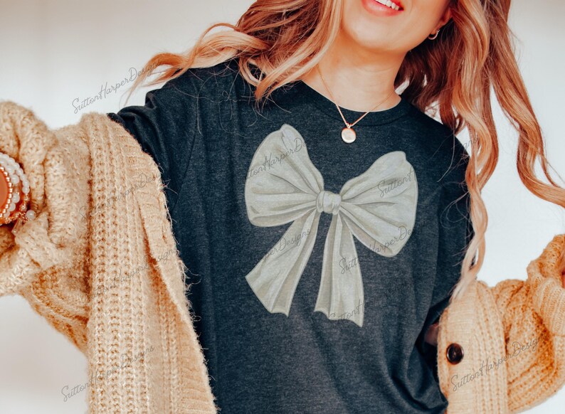 May include: A dark gray t-shirt with a large white bow design. The bow is painted in a watercolor style.