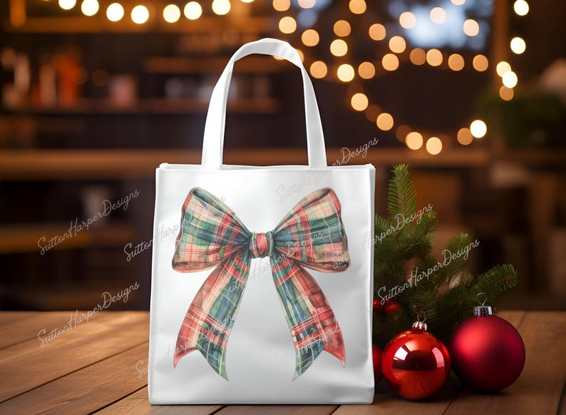 May include: White tote bag featuring a large red, green and white plaid bow. The bow is tied in a knot with the ends hanging down. The bag is placed on a wooden surface.