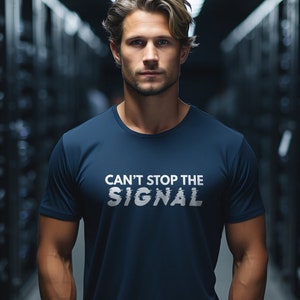 May include: A navy blue t-shirt with the text "CAN'T STOP THE SIGNAL" in white. The shirt is being worn by a person in a server room setting.