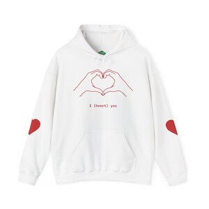 May include: White hoodie with a red heart design on the sleeves and a red line drawing of hands forming a heart on the front. The text "I (heart) you" is below the heart graphic. The hoodie has a front pocket and a drawstring hood.