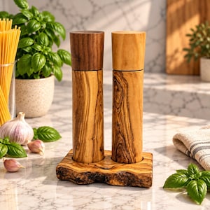Könnte beinhalten: Zwei zylindrische Salz- und Pfeffermühlen aus Holz auf einem passenden rechteckigen Holzsockel mit natürlicher Baumkante. Eine Mühle hat einen dunkelbraunen Aufsatz, die andere einen hellen Holzaufsatz, beide mit sichtbarer Maserung.