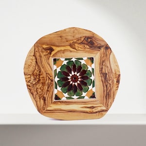 May include: A round olive wood serving tray with a square tile inset. The tile is decorated with a geometric pattern in shades of green, brown, and white.