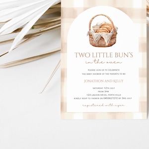 May include: A baby shower invitation with a gingham background and a basket of bread rolls. The text reads "Two Little Bun's in the Oven".