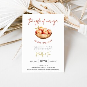 May include: A baby shower invitation with a watercolor illustration of red apples in a bowl. The text reads "the apple of our eye is on it's way". The invitation is for Madly & Tim on Sunday, August 18th from 10am to 3pm at 88 Lagoon Drive, Perth WA. RSVP to Polly at 0453627272.