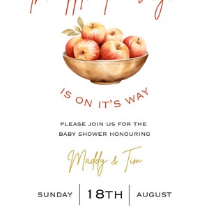 May include: A baby shower invitation with a red apple theme. The invitation features a bowl of red apples with green leaves and the text "the apple of our eye is on it's way". The invitation also includes the text "Please join us for the baby shower honouring Maddy & Tim", "Sunday 18th August", "10am - 3pm", "88 Lagoon Drive, Perth WA", and "Kindly RSVP to Polly on 0453627272".