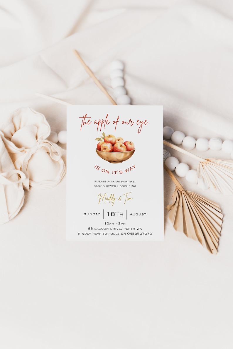 May include: A baby shower invitation with a watercolor illustration of a bowl of red apples. The text reads "The apple of our eye is on it's way." The invitation is for a baby shower honoring Maddy & Tim on Sunday, August 18th from 10am to 3pm at 88 Lagoon Drive, Perth WA. RSVP to Polly at 0453627272.