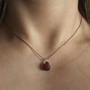 May include: A silver chain necklace with a dark red gemstone pendant.