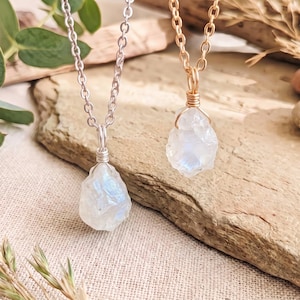 Puede incluir: Dos collares con colgantes de piedra lunar en bruto y translúcida. Un colgante está envuelto en alambre plateado con una cadena a juego, mientras que el otro está envuelto en alambre dorado con una cadena dorada a juego.