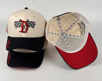 May include: Two baseball caps. One is cream-colored with a black brim, a red letter "D" and checkered flags. The other cap has a red brim and a cream-colored interior. The caps have the text "Lightning McQueen" on the side.