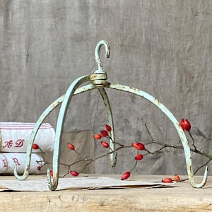 May include: A vintage, pale blue metal hanging rack with a curved design and four hooks. The rack has a distressed, aged appearance. Red berries on a branch are placed near the rack, adding a pop of colour. The rack is likely for decorative purposes.