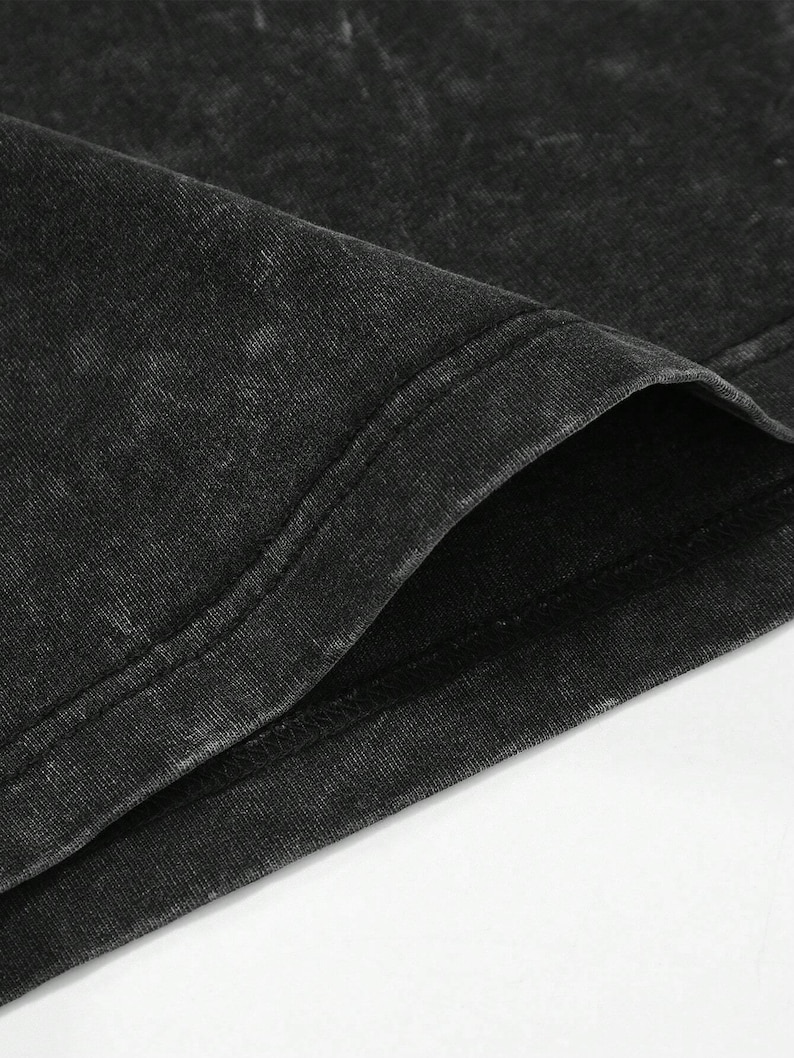 Puede incluir: Primer plano de una camiseta negra con lavado &aacute;cido. La tela tiene un aspecto texturizado con &aacute;reas m&aacute;s claras, creando un efecto descolorido. Se ve el cuello, con una costura de doble pespunte. La camiseta est&aacute; hecha de un material suave y c&oacute;modo.