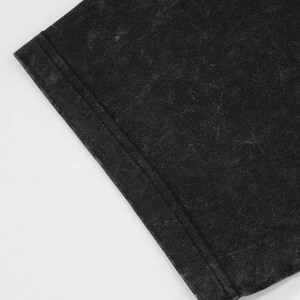Puede incluir: Primer plano de una tela negra deste&ntilde;ida, probablemente una camiseta. La tela tiene un aspecto texturizado con costuras visibles en el borde. El color es un negro descolorido con &aacute;reas m&aacute;s claras, creando un aspecto vintage.
