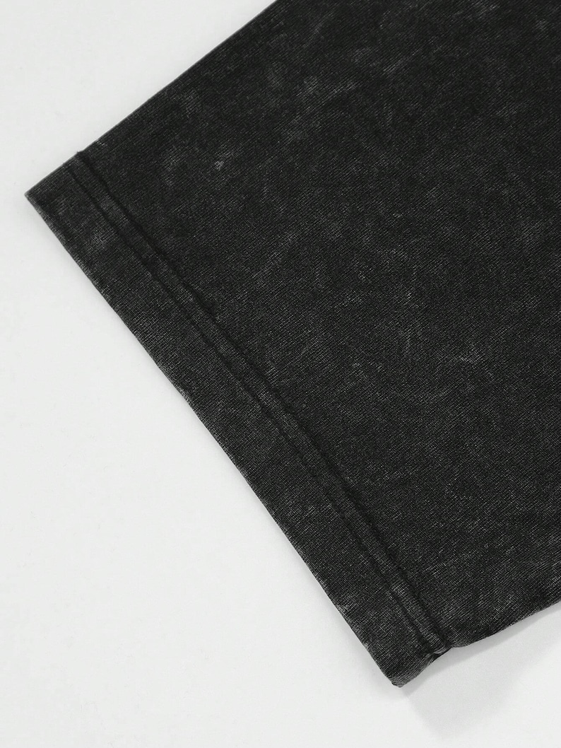 Puede incluir: Primer plano de una tela negra deste&ntilde;ida, probablemente una camiseta. La tela tiene un aspecto texturizado con costuras visibles en el borde. El color es un negro descolorido con &aacute;reas m&aacute;s claras, creando un aspecto vintage.