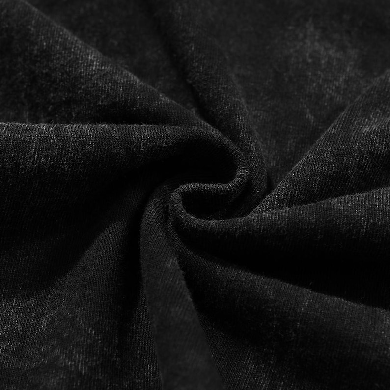 Puede incluir: Primer plano de tejido vaquero negro con un aspecto texturizado y ligeramente descolorido. El tejido est&aacute; tejido apretado, con l&iacute;neas diagonales visibles y sutiles variaciones de tono, creando una sensaci&oacute;n de profundidad y dimensi&oacute;n. El tejido est&aacute; doblado, mostrando la textura y la forma en que la luz incide en el tejido.