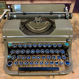 May include: A vintage green Underwood typewriter with a black keyboard and blue keys. The typewriter has a metal body and a silver carriage return lever.