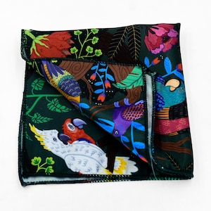 May include: A dark green pocket square with a colorful parrot and floral print. The square features a detailed design of parrots, flowers, and foliage in shades of red, blue, purple, and yellow. The edges are finished with a black border.