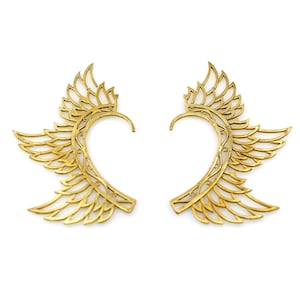 May include: A pair of gold-tone ear cuffs with a wing design. The cuffs are made of metal and have a delicate, intricate design.