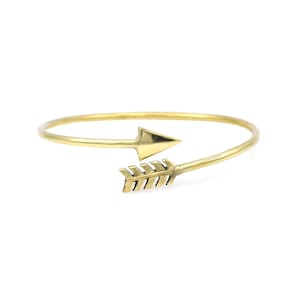 May include: A gold-toned arrow bracelet with a simple design. The bracelet is made of a thin metal band with a small arrowhead at one end and a fletched arrow at the other.