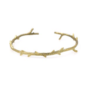 May include: A gold-toned bangle bracelet with a delicate design of intertwined branches.