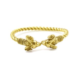 May include: A gold-toned twisted bangle bracelet with ram's head ends. The ram's heads are facing each other and have detailed horns.