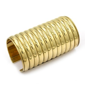 May include: A gold-toned metal bracelet with a coiled design. The bracelet is made of multiple overlapping bands.