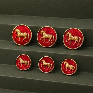 May include: A set of six circular buttons featuring a textured red background with a raised gold-toned horse figure in the center. The buttons are arranged in two rows, with three larger buttons on top and three smaller buttons on the bottom.