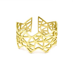 Op de afbeelding: Een gouden metalen armband met een geometrisch patroon. De armband is open en heeft een golvende, gekartelde rand.