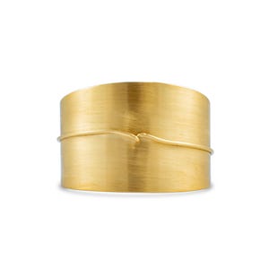May include: A gold-toned metal cuff bracelet with a wavy line design.