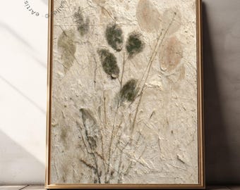 May include: A framed botanical art print with a textured, cream-coloured background. The print features pressed plant elements in green, brown, and beige. The artwork is set within a thin, gold-toned wooden frame, offering a natural aesthetic.