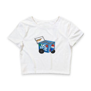 May include: White crop top featuring a colorful graphic of an ice cream cart with the text "UCK ICE". The cart is blue with black wheels and a red, white, and blue popsicle. The cart has a metal handle.