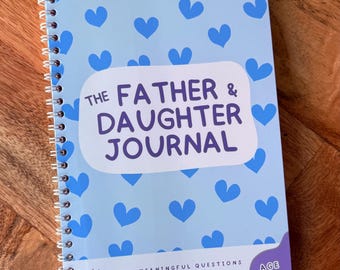 May include: A spiral-bound journal with a light blue cover featuring a pattern of dark blue hearts. The text reads: The Father & Daughter Journal, with meaningful questions and fun activities to complete together, age 7-12.