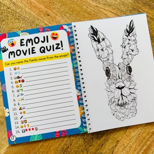 May include: A blue and yellow book with the text "Emoji Movie Quiz!" and a list of numbers with emojis next to them. The book is open to a page with a black and white drawing of a rabbit with flowers on its head.