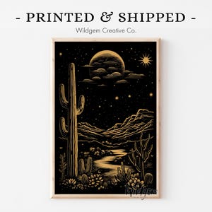 Framed black and gold western cactus print featuring a bold saguaro under a glowing moon and starry sky, displayed on a white wall with “PRINTED & SHIPPED – Wildgem Creative Co.” above.