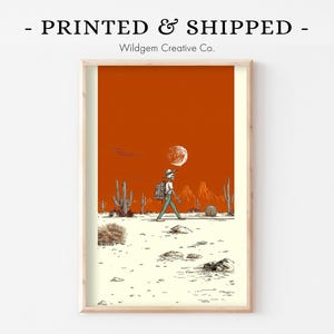 Unframed print held in cozy sweater-clad hands atop a soft fabric surface, styled as a giftable, ready-to-frame piece of art.