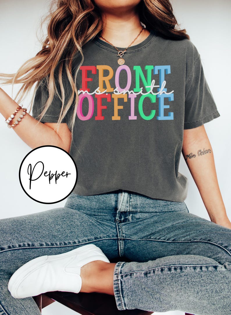 Pu&ograve; includere: Una maglietta grigia scura con il testo "FRONT OFFICE" in colori arcobaleno. Il testo &egrave; in un font di scrittura a mano.