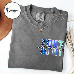 May include: Gray t-shirt with a blue, green, and purple graphic that says "CRUT Hannah".