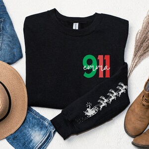 May include: Black sweatshirt with a green and red "911 emma" graphic on the front and a white reindeer design on the sleeve.