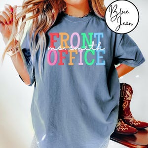 Pu&ograve; includere: Una t-shirt blu jeans con il testo "FRONT OFFICE" in colori arcobaleno. Il testo "no smith" &egrave; scritto in bianco corsivo sopra la parola "OFFICE".