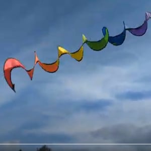 May include: A rainbow colored kite flying in a blue sky with white clouds. The kite is shaped like a long, thin, spiral.
