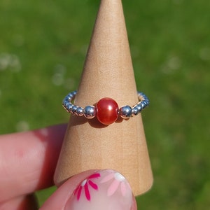 May include: A silver beaded ring with a single red gemstone.