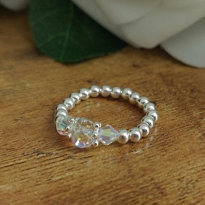 May include: A silver ring with a beaded band and three iridescent crystal accents.