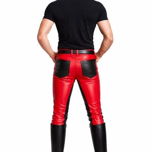 May include: Red leather pants with black accents and a black belt. The pants have black panels on the sides and back pockets. The person is also wearing a black t-shirt and black knee-high boots.