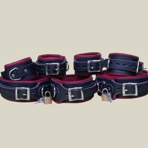 May include: A set of black leather restraints with silver buckles and red padding. The set includes wrist cuffs, ankle cuffs, and a neck collar, each with a small padlock and key.