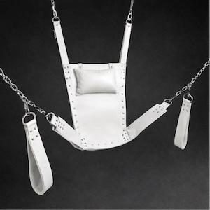 May include: A white leather swing with a small pillow and riveted accents. The swing is suspended by metal chains and features attached straps with handles. The background is a dark, solid color.