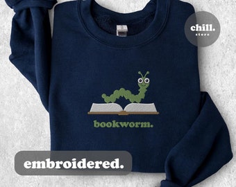 May include: Navy blue sweatshirt with an embroidered green bookworm design. The bookworm is wearing glasses and is reading a book. The text "bookworm." is embroidered below the bookworm. The text "embroidered." is printed below the design.